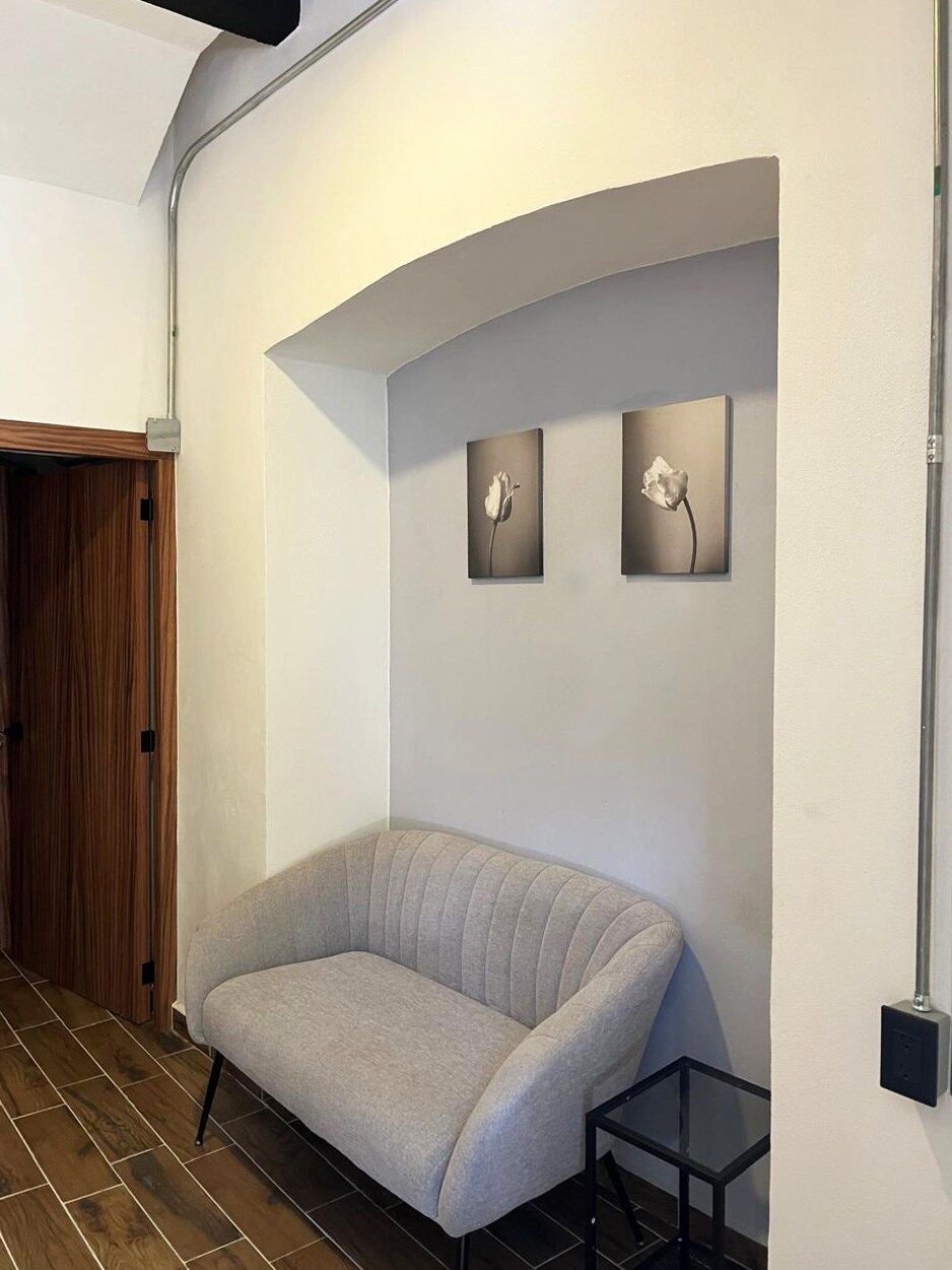 Quarto com sofá cinzento, porta de madeira e duas molduras na parede.