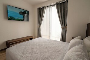 A bedroom with a bed, a TV mounted on the wall, and a window with curtains. - Laurelian 2 · Aure · Private suite near downtown (Oaxaca de Juárez)