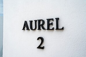 Een huisnummerbord met 'AUREL 2' bevestigd aan een structuurrijke muur.