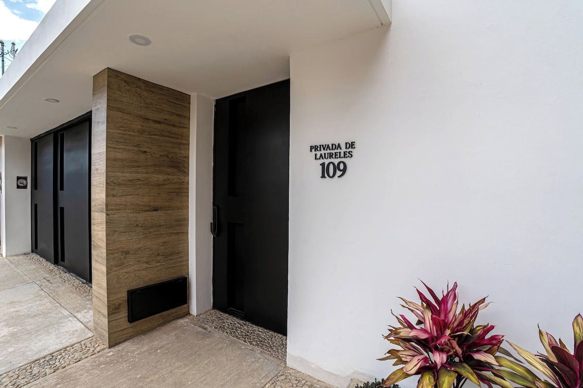 Ein moderner Gebäudeeingang mit einer Wand aus Holz, einer schwarzen Tür und einem Schild mit der Aufschrift 'PRIVADA DE LAURELES 109'.