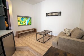A modern living room with a wooden floor, a sofa, a coffee table, a bench, a television, and a wall-mounted decorative piece. - Laurelian 6 · Vare · Private suite near downtown (Oaxaca de Juárez)
