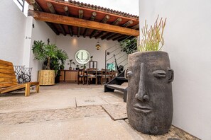 Un pati exterior amb sòl de pedra, mobles de fusta, una gran jardinera amb un disseny semblant a un rostre, i un sostre d'aquarelles.