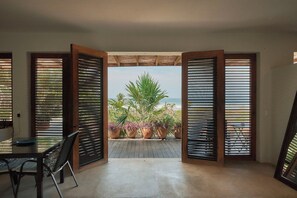 A room with a view of the ocean, featuring a wooden table and chairs, and potted plants.