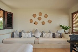 A modern living room with a sofa adorned with striped and polka dot cushions, a wall-mounted woven art piece, and a potted plant.