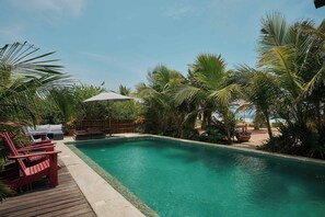 A clear blue pool surrounded by palm trees and wooden deck chairs.