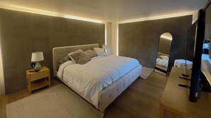 Ein modernes Schlafzimmer mit einem großen Bett, Nachttischen, einem Spiegel und einem Fernseher.