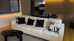 Ein modernes Wohnzimmer mit einem weißen Sofa, schwarzen Kissen, einem schwarzen Couchtisch und Holzboden.