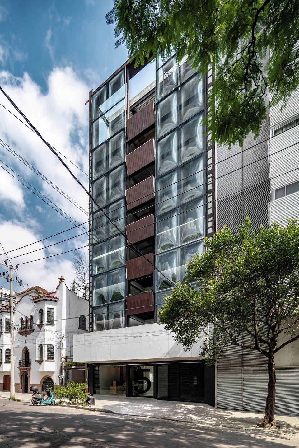 A modern building with a glass facade, a tree in the foreground, and a scooter parked outside.