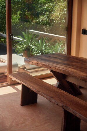 A wooden bench with a slatted design, positioned in a room with a view of greenery through a glass door. - Ocean View Suite w/ Rooftop & Pool Access (Puerto Escondido)