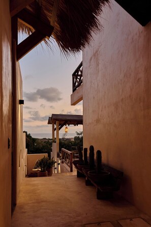 A covered outdoor area with a thatched roof, potted plants, and a view of the sea. - Ocean View Suite w/ Rooftop & Pool Access (Puerto Escondido)