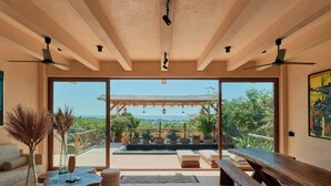 Il s’agit d’une pièce spacieuse dotée d’une grande porte-fenêtre coulissante qui donne sur un patio extérieur avec une piscine et des plantes. À l’intérieur, on trouve un banc en bois et un canapé.