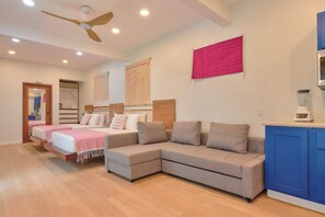 A modern bedroom with two beds, a sofa, a ceiling fan, and a kitchenette. - Suite in La Punta, a minute from the sand (Puerto Escondido)