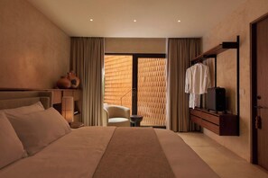 A hotel room with a large bed, a seating area with a chair, a small table, a wardrobe, and a view through a window with a patterned blind. - Luxury Boutique Hotel in Downtown Oaxaca (Oaxaca de Juárez)