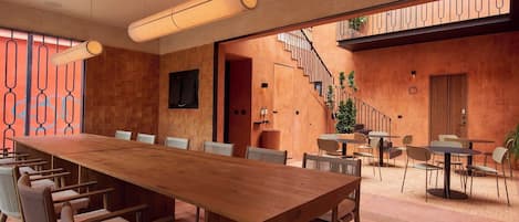 A spacious indoor area with a long wooden table and chairs, a staircase, and a balcony with plants.