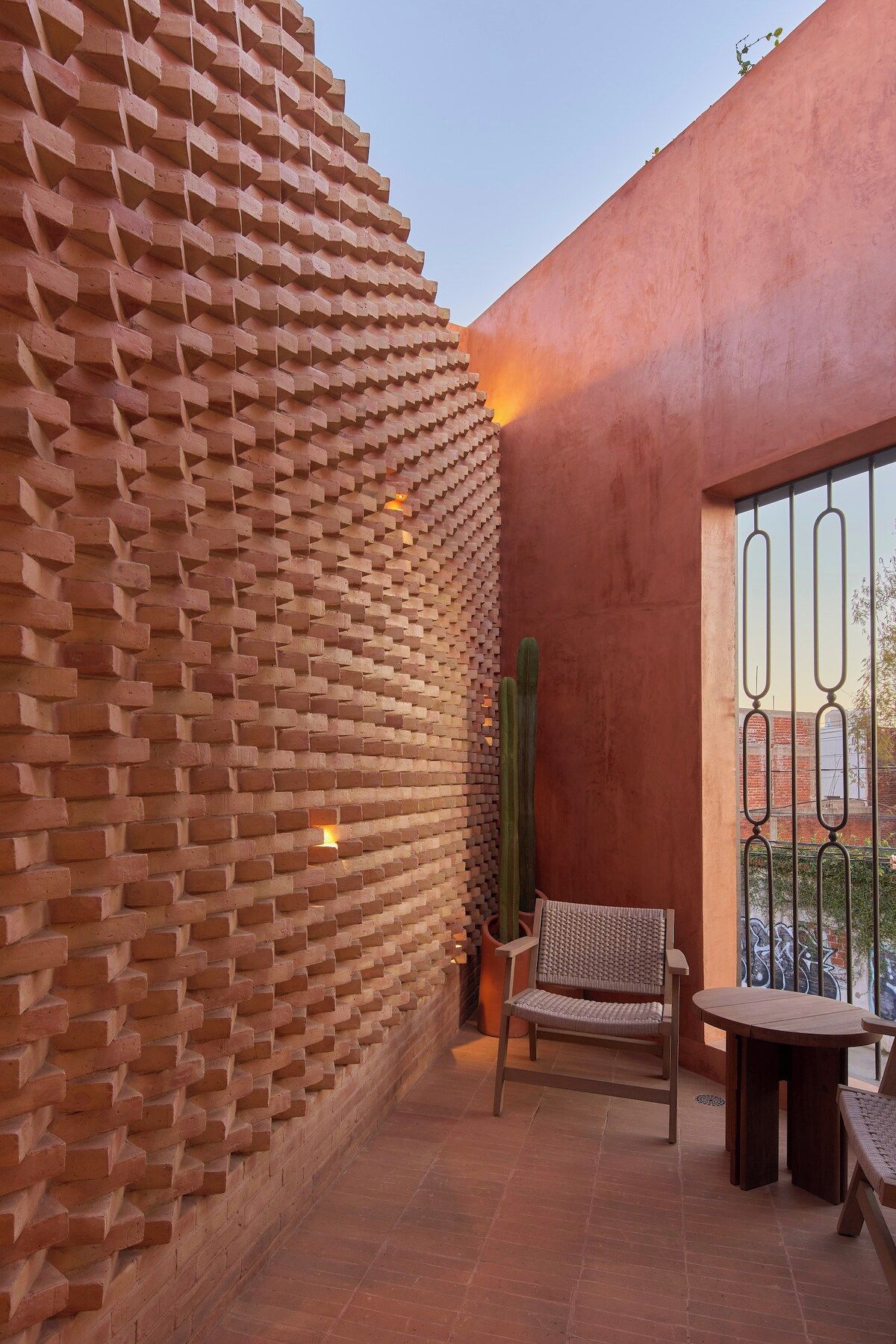 A brick wall with a cactus and a chair in a patio area.