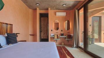 Ein Schlafzimmer mit einem großen Bett, einem Holz-Kopfstück, einem Nachttisch, einem Fenster mit Blick und einem Badezimmer mit Waschbecken, Spiegel und Handtuchhalter.