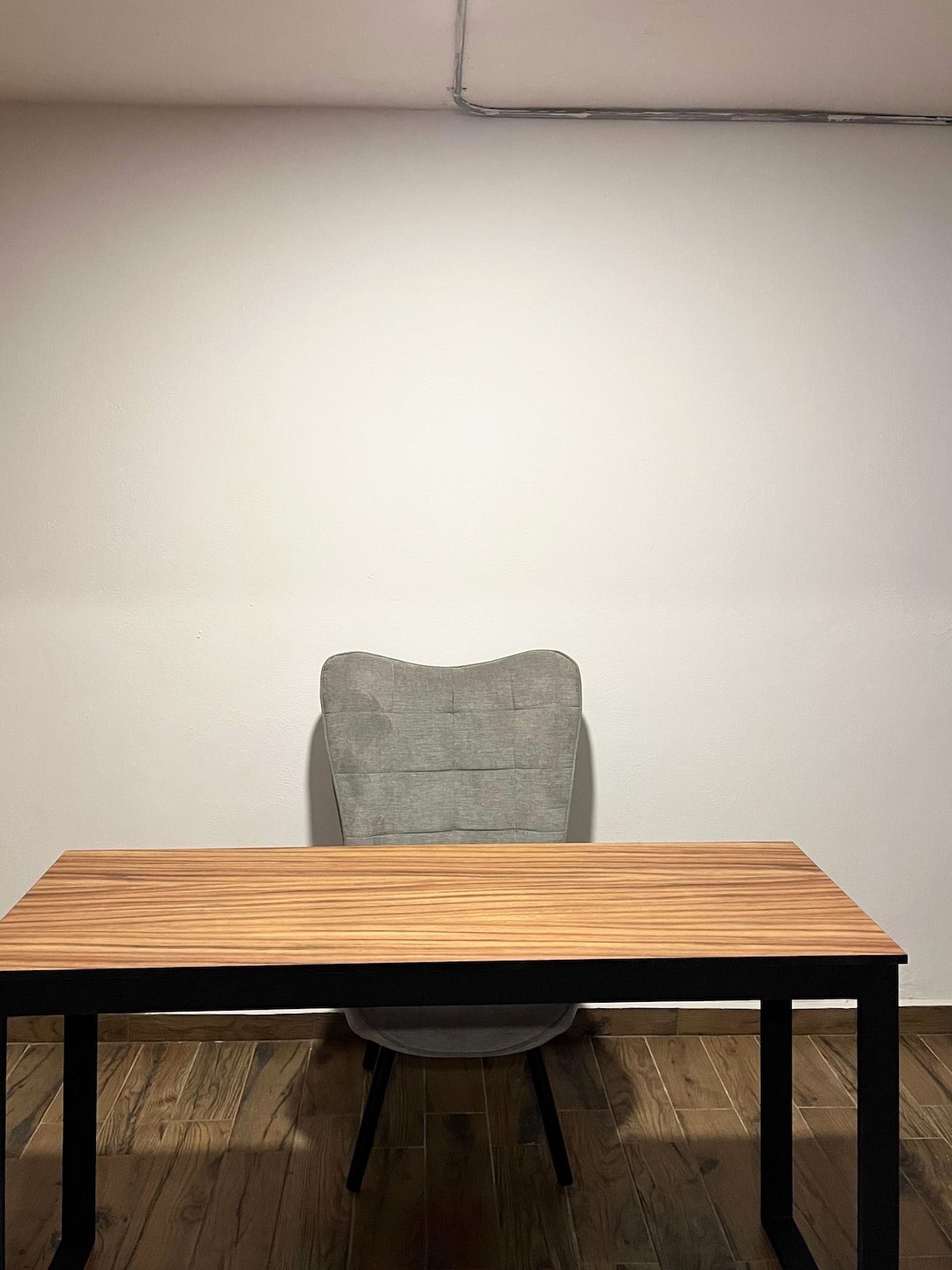 A wooden table with a chair in front of a plain wall.