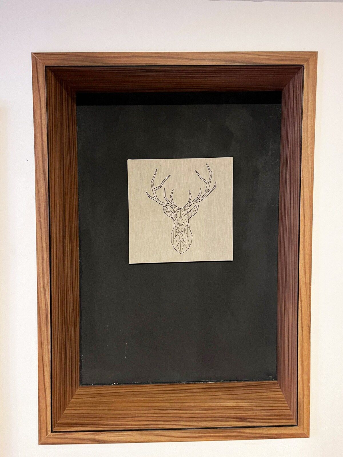 Ein gerahmtes Kunstwerk, das einen Hirschkopf vor schwarzem Hintergrund zeigt.