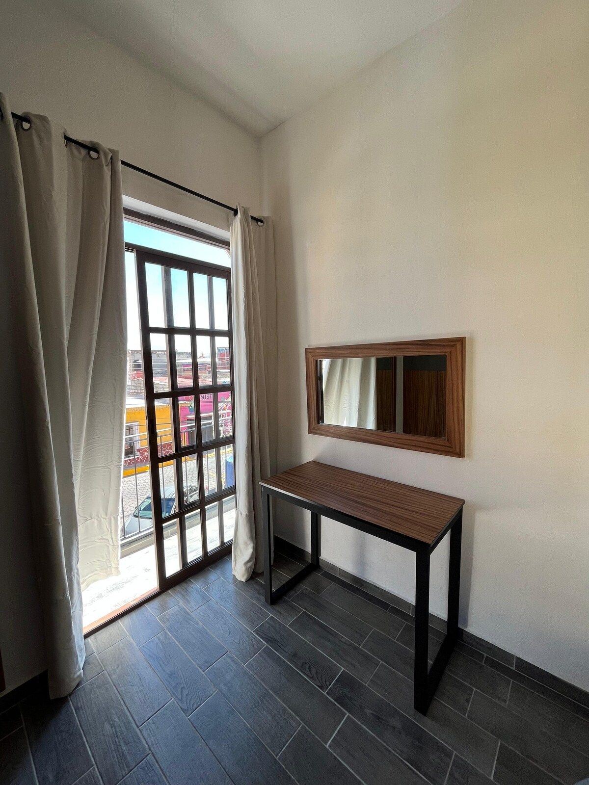 A room with a window, a table, and a mirror.