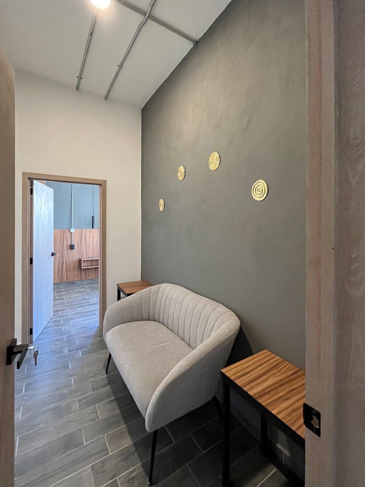 Quarto moderno com sofá curvo, pequena mesa de madeira e parede cinza decorada com pratos.