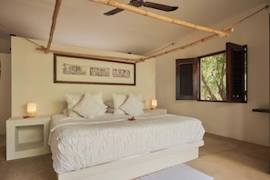A bedroom with a bed, bedside lamps, framed artwork, a window with shutters, and a ceiling fan.