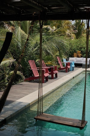 A pool area with red lounge chairs, a swing, and a grey sofa.
