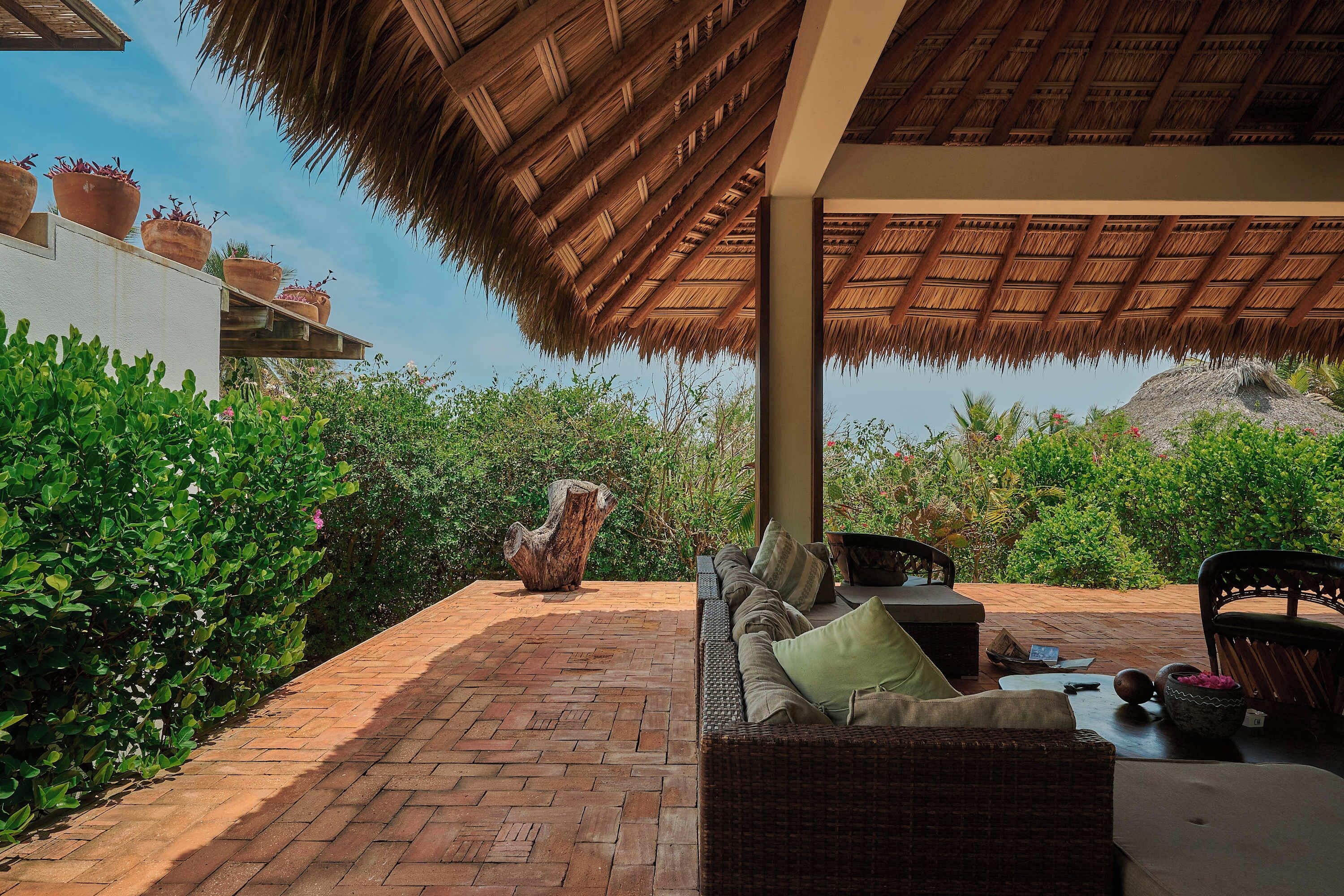 An outdoor seating area with a thatched roof, wicker furniture, and potted plants.