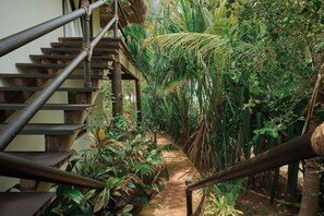 Un escalier en bois, doté de rampes en métal, longe un sentier verdoyant au cœur d’un jardin luxuriant.