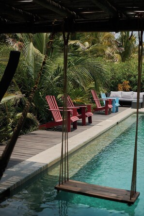 Un espace piscine avec des chaises longues rouges, une balançoire et un canapé gris.