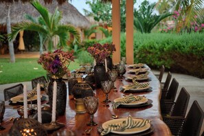 An outdoor dining area with a long wooden table set for a meal, surrounded by chairs, and decorated with vases of flowers and candles. - Casa Juliana · Private suite · Beachfront property (Puerto Escondido)