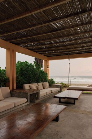 An outdoor seating area with a view of the ocean, featuring a wooden table, a sofa, and a swing. - Casa Juliana · Private suite · Beachfront property (Puerto Escondido)