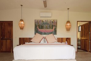 A hotel room with a large bed, two wall-mounted lamps, a painting, and wooden doors. - Casa Juliana · Private suite · Beachfront property (Puerto Escondido)