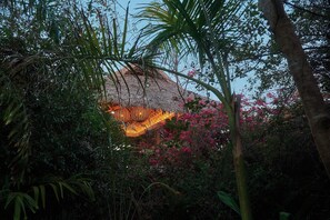 A thatched-roof structure surrounded by dense foliage and flowering plants. - Full Beachfront Estate · Jungle & Pacific (Puerto Escondido)