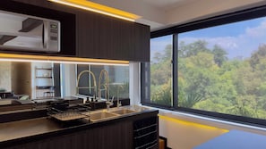 A modern kitchen with a built-in microwave, stainless steel sink, and a window with a view of trees. - Eighth floor facing Parque España, Condesa (Ciudad de México)