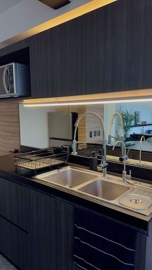 Une cuisine moderne avec des meubles de couleur sombre, un évier en acier inoxydable et un four à micro-ondes encastré.