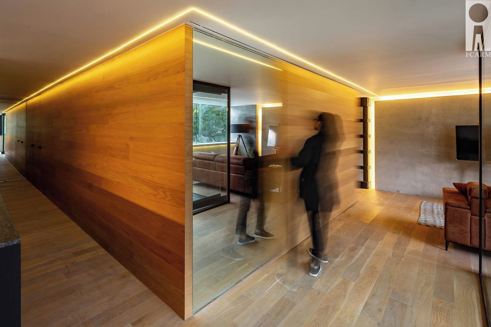 A modern interior with a wooden partition, a sofa, a television, and a person walking.