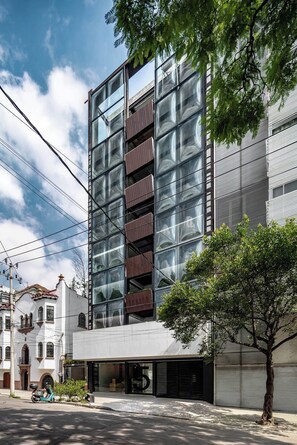 A modern building with a glass facade, a tree in the foreground, and a scooter parked outside. - Eighth floor facing Parque España, Condesa (Ciudad de México)