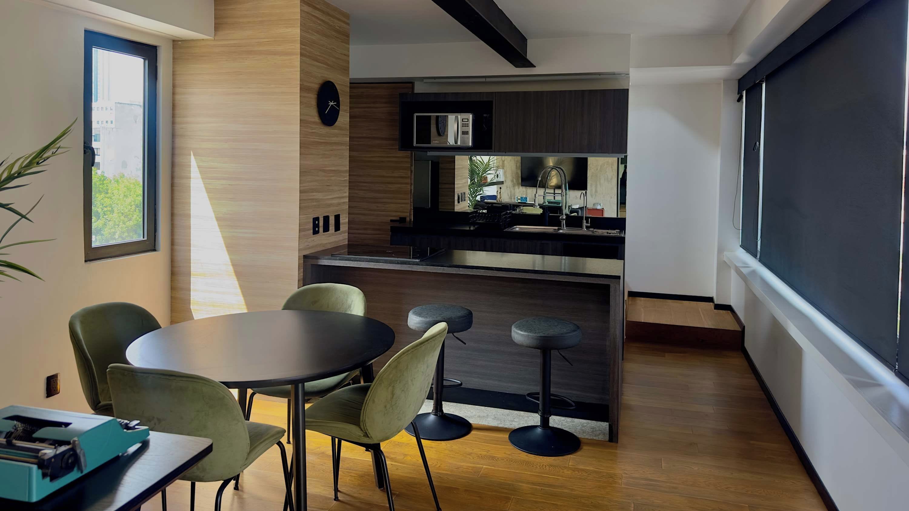 A modern kitchen with a microwave, sink, and bar stools. There is a dining area with a table and chairs.