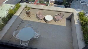 Une terrasse sur le toit avec une table ronde, deux chaises, une petite plante en pot et un coin salon comprenant un banc et deux chaises.