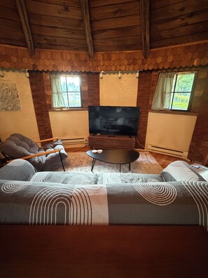 A cozy living room with a wooden ceiling, a large sofa, a coffee table, and a television.