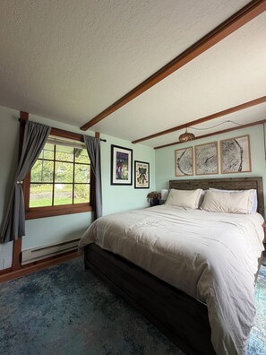 A bedroom with a large bed, a window with curtains, and framed artwork on the wall.
