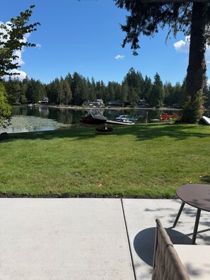 A grassy area with a dock, boats, and a lake surrounded by trees.