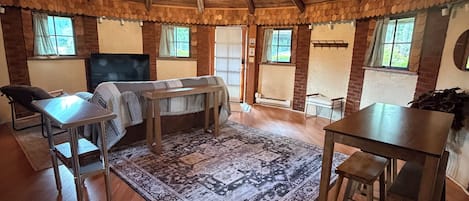A spacious room with a high wooden ceiling, a chandelier, a large rug, and a television.