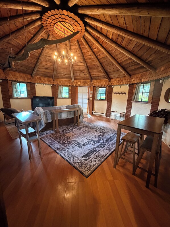 A spacious room with a high wooden ceiling, a chandelier, a large rug, and a television.