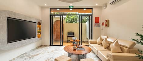 A modern lobby with a flat-screen TV, a round coffee table, a sofa, and a glass door leading outside.