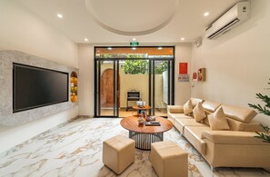 Een moderne lobby met een flatscreen televisie, een ronde salontafel, een bank en een glazen deur naar buiten.