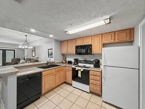 A modern kitchen with wooden cabinets, a black microwave, a white refrigerator, and a dishwasher. - The Fairway Retreat | Golf Course Views | Pool & Spa | Dollywood (Pigeon Forge)