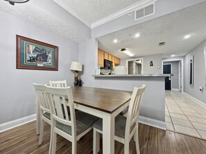 A dining area with a wooden table and white chairs, a framed picture on the wall, and a kitchen in the background. - The Fairway Retreat | Golf Course Views | Pool & Spa | Dollywood (Pigeon Forge)