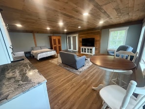 Ein geräumiges Zimmer mit Holzbalkendecke, einem Esstisch mit Stühlen, einer Couch und einem Fernseher.