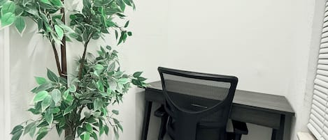 A corner office with a black desk and chair, a potted plant, and white walls.